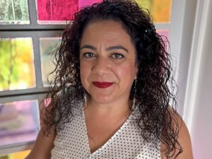 Brock professor Cristina Santos smiles in front of a colourful window.