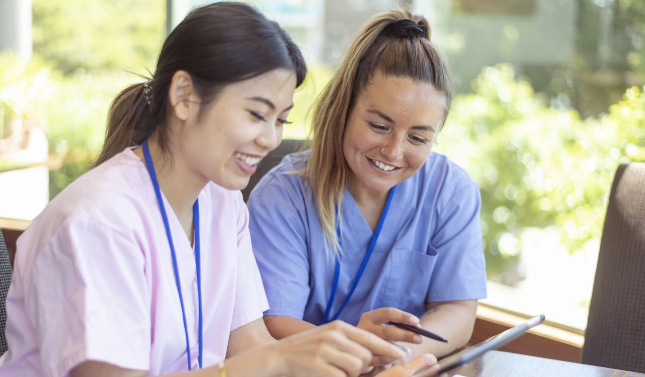 Two young nurses look at a tablet together.