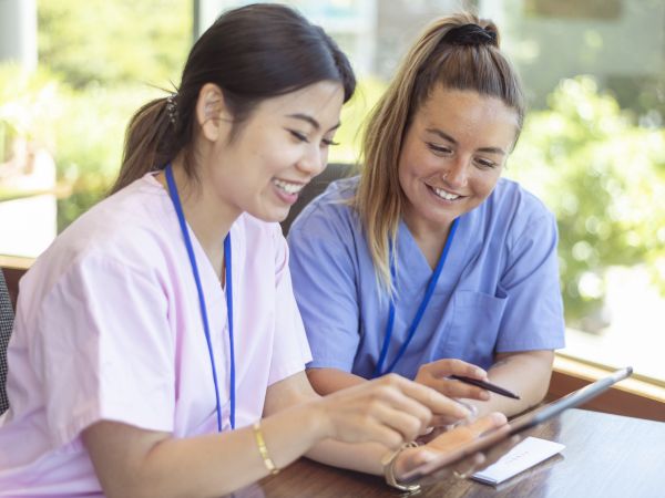 Two young nurses look at a tablet together.