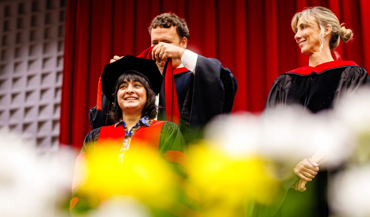 A man places a graduation hood over the shoulders of a new graduate at Convocation ceremony.