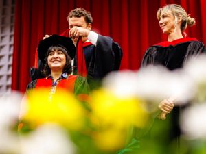 A man places a graduation hood over the shoulders of a new graduate at Convocation ceremony.