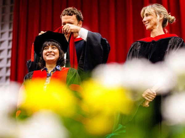 A man places a graduation hood over the shoulders of a new graduate at Convocation ceremony.