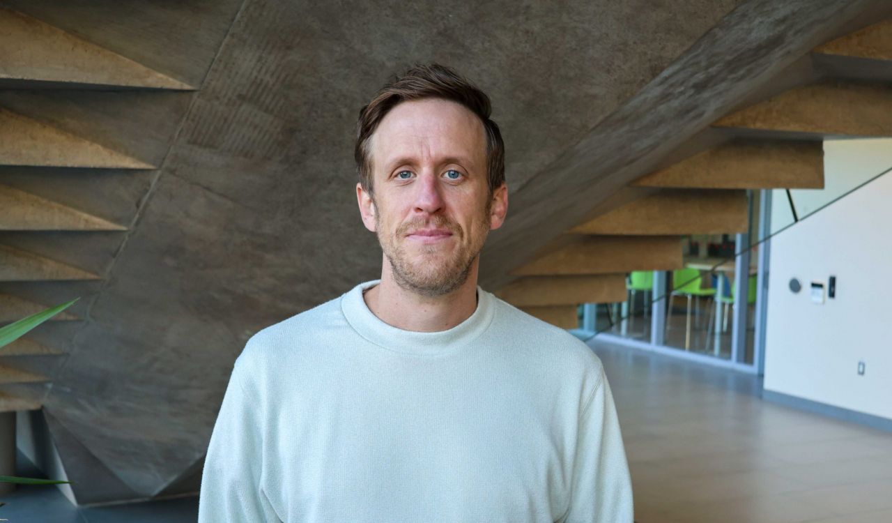 A man stands in a sunny university hallway.