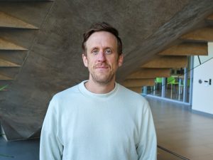 A man stands in a sunny university hallway.