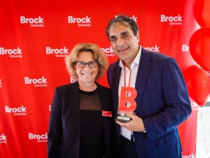 A woman and a man, holding a trophy, pose in front of a red backdrop.