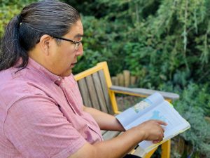 Joshua Manitowabi sits outside at Brock University reading a book containing a map.