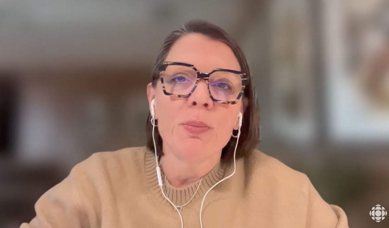A screenshot from a CBC podcast video of a female guest sitting in an office, wearing glasses and headphones.