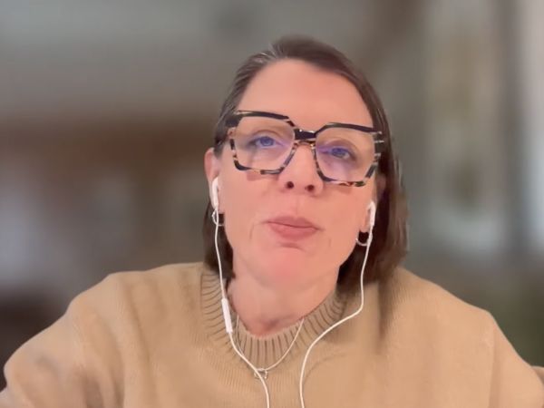 A screenshot from a CBC podcast video of a female guest sitting in an office, wearing glasses and headphones.