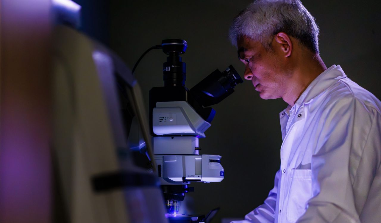 A man in a lab coat looks into a microscope.