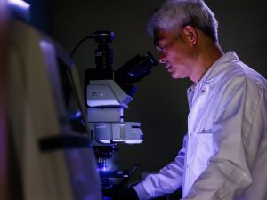 A man in a lab coat looks into a microscope.