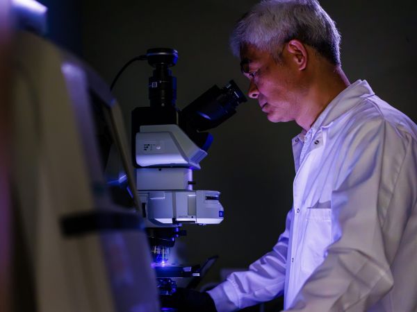 A man in a lab coat looks into a microscope.