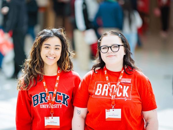 Two people in Brock University-branded shirts stand together in a busy room filled with people.