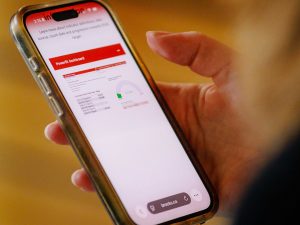 Close-up of a person holding a smartphone displaying a Brock University PowerBI dashboard, with charts and performance metrics visible on the screen against a blurred indoor background.