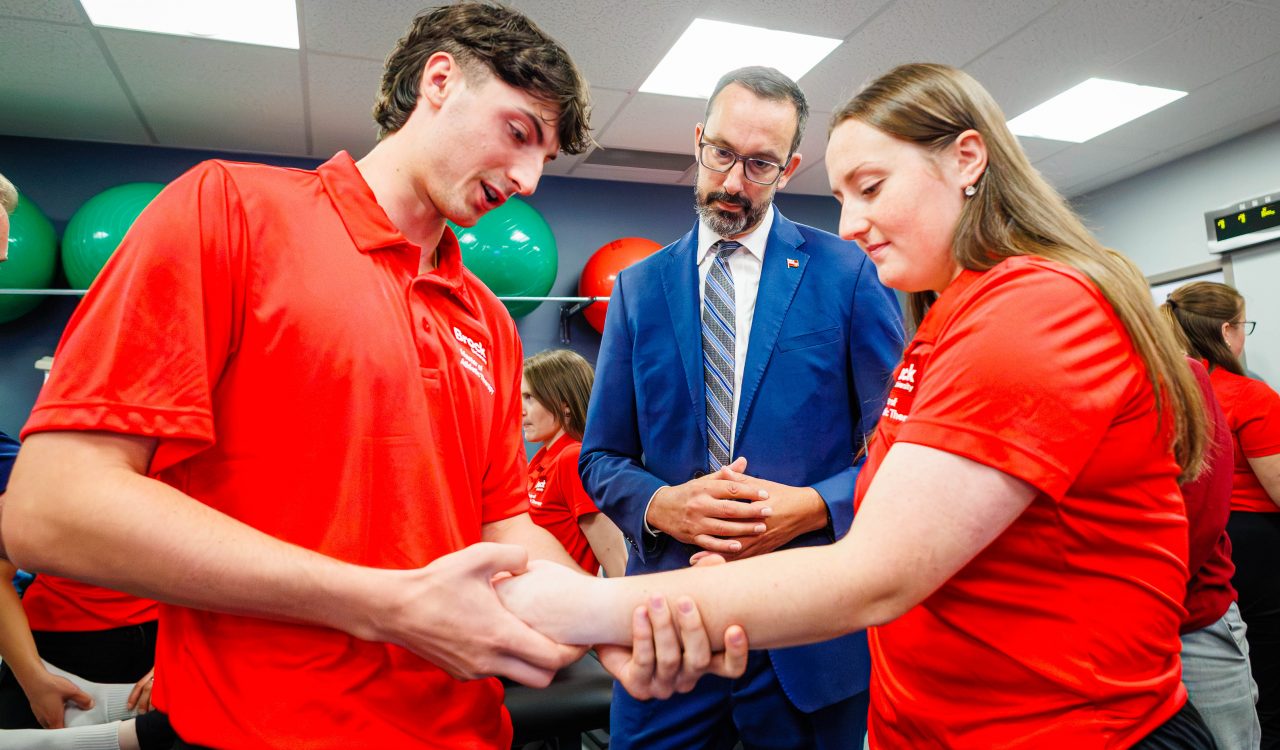 First-year MAT students Zach Perna and Olivia Nero demonstrate musculoskeletal assessment techniques with Minister Nolan Quinn inside Brock's campus anatomy lab.