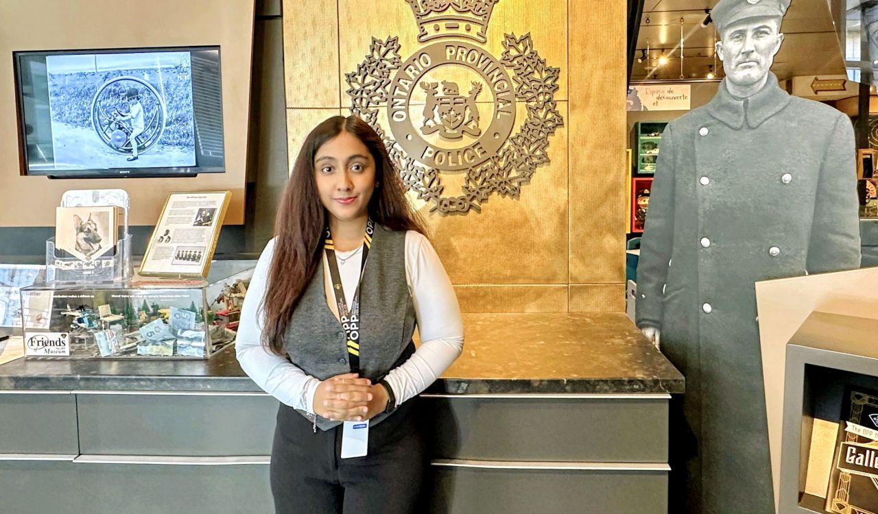 A woman, with a staff lanyard hanging around her neck, stands in front of a branded sign at the Ontario Provincial Police headquarters.