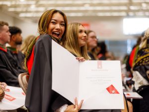 A woman in a graduation gown holds open a folder containing her Brock University degree.