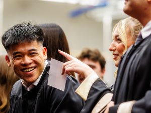 Graduates smile while sitting in an auditorium.