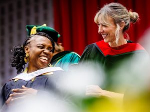 Two women in Convocation gowns smile at one another.