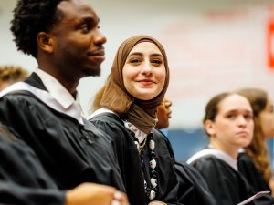 A group of graduates are pictured seated in a gymnasium.