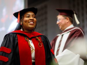 A woman in a graduation gown walks across the Convocation stage.