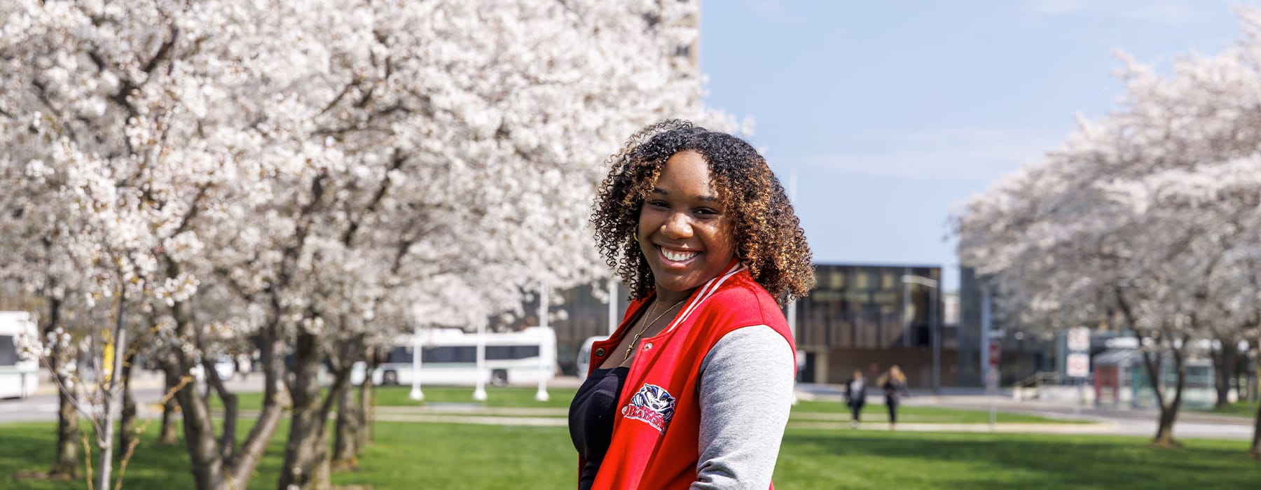 Student wearing a Brock Badgers jacket in front of schmon tower and cherry blossoms