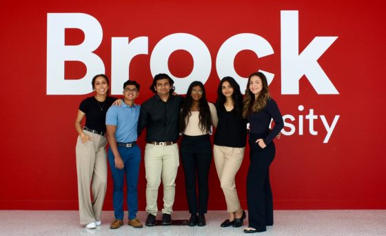 group of students in fron of the Brock University logo on a red wall