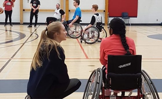 Law Plus volunteer with a person in wheelchair in a gym