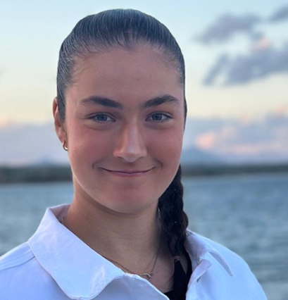 Young women with dark hair in a braid, wearing a white shirt in front of a lake
