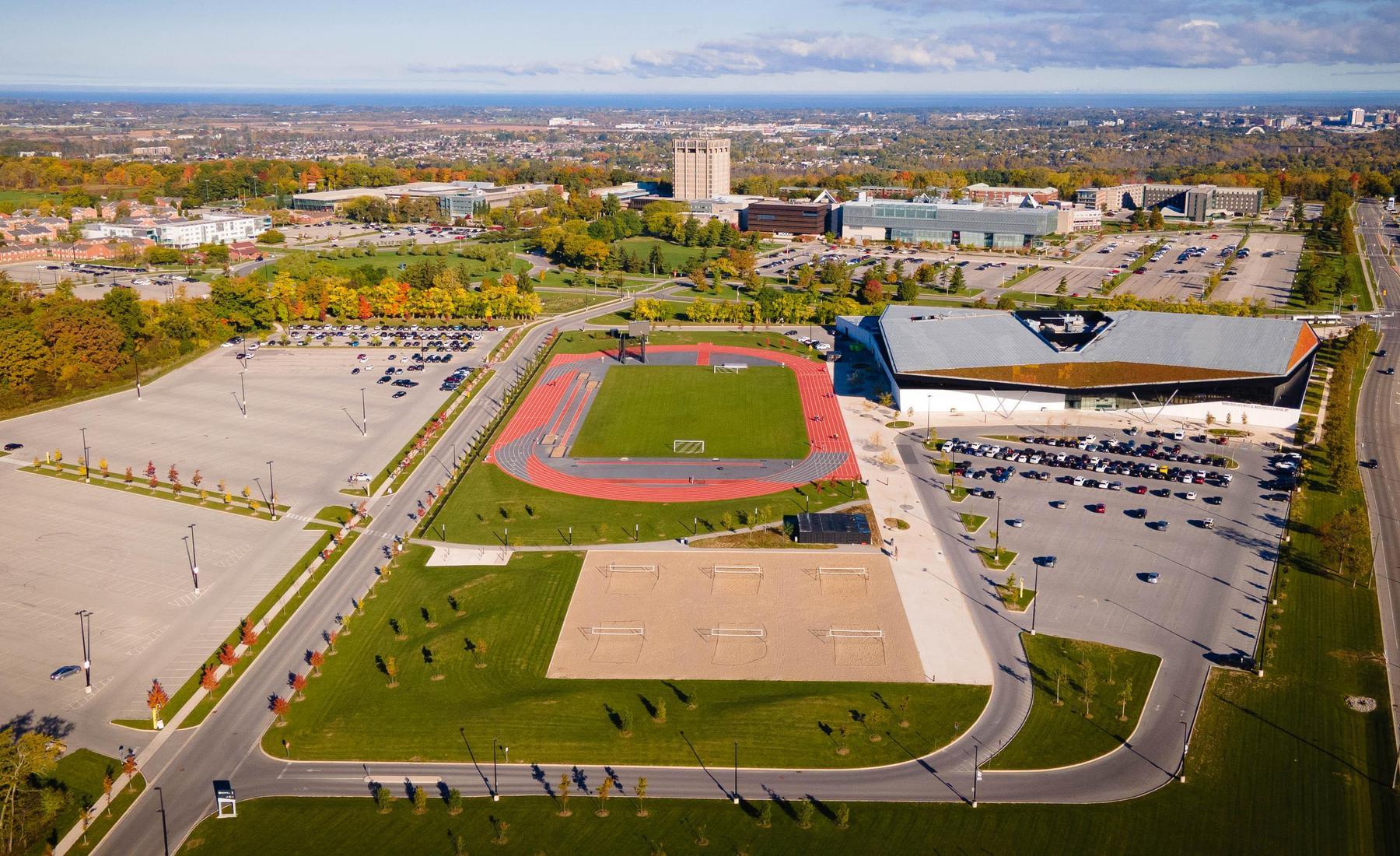 Aerial image of Canada Games Park, including parking lot, athletic track, beach volleyball courts, and venue building. Brock University's campus in the background. 
