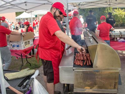 food service worker in a red shirt grills sausages