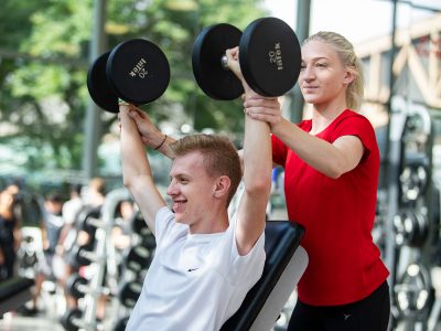 Personal trainer helping student lift weights at Brock University