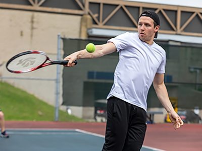 Student hitting a tennis ball on the tennis courts at Walker Sports Complex
