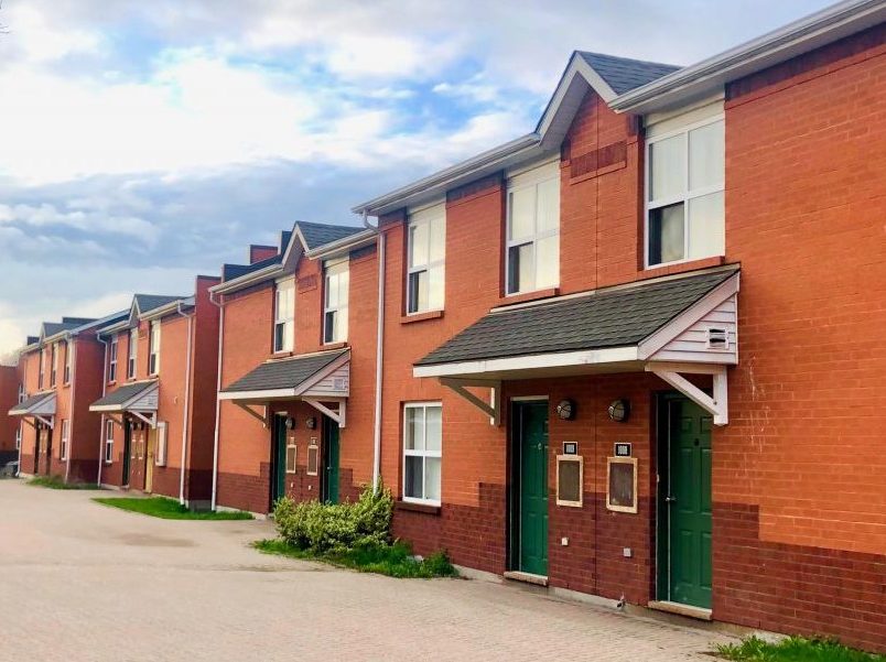 Exterior image of Village Residence Townhouse court at Brock University. Series of townhouse units grouped together, with a shared pathway and grassy area in front of the units.