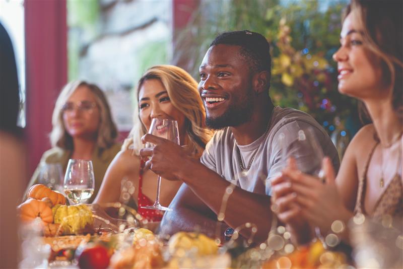 group of young adults sitting at a table holding wine glasses 