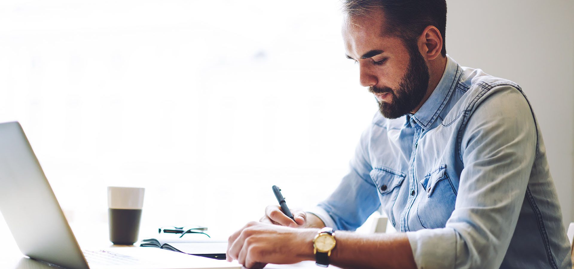 Man at desk in front of window with laptop