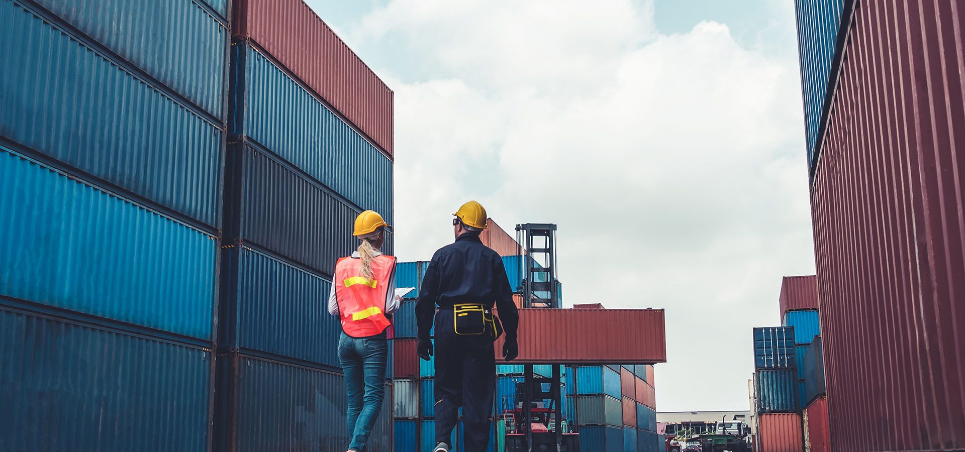 two people wearing hardhats in a container shipyard