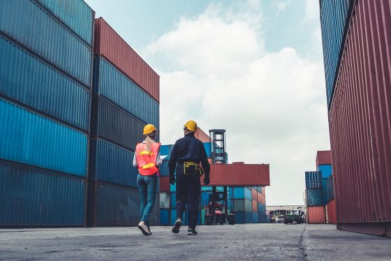 two people wearing hardhats in a container shipyard