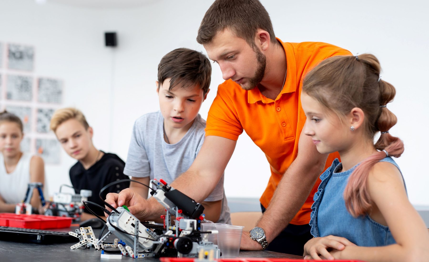 Male teacher in classroom with young students around him in tech class 