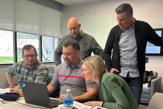 group of adult learners at a desk looking at laptop