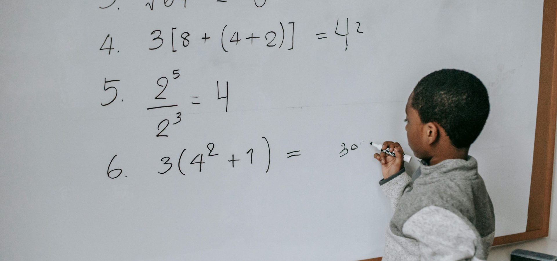 A young boy doing math on a classroom whiteboard