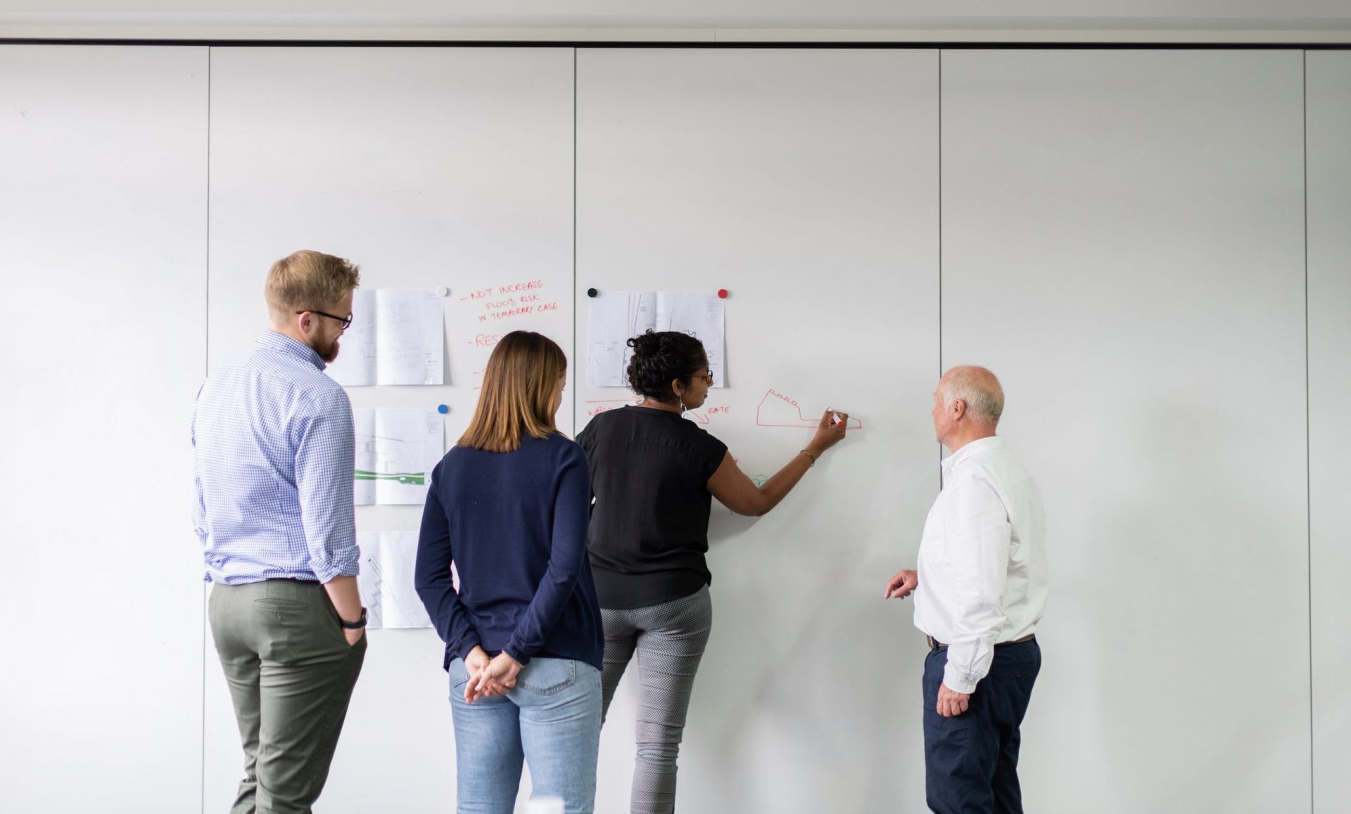group of people standing up around whiteboard and one writing