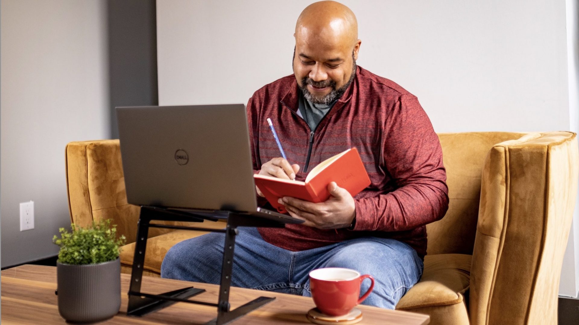 person writing on notebook in front of laptop