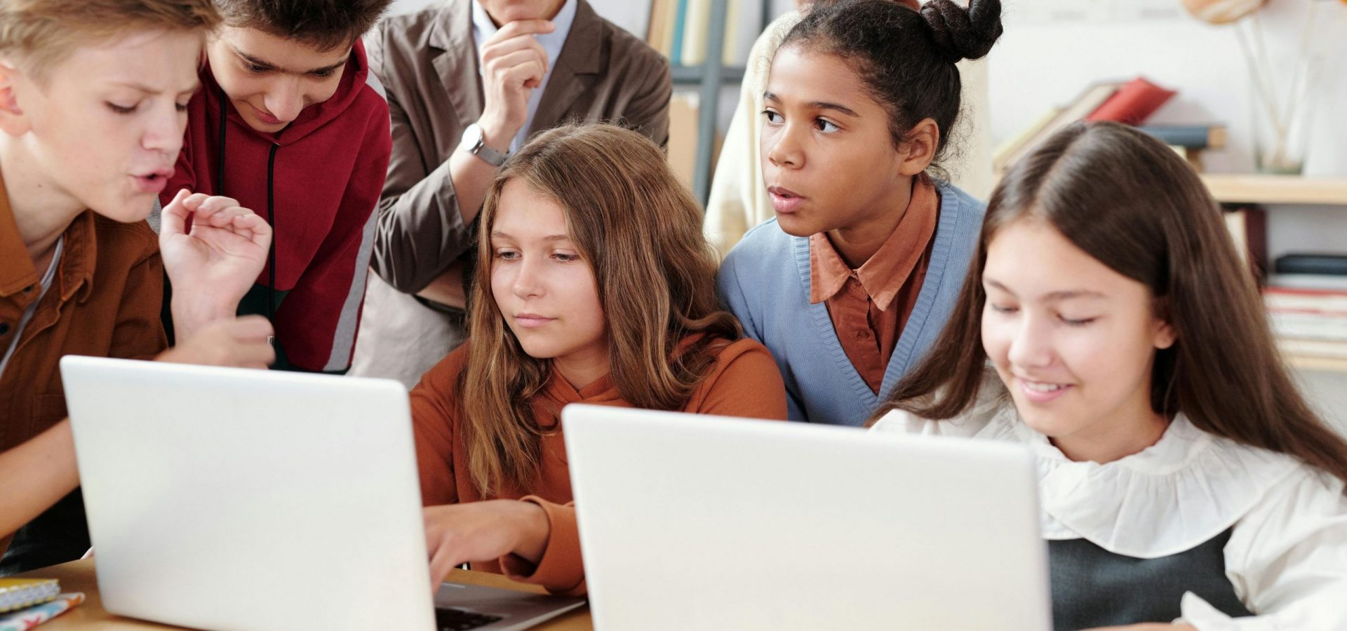 A group of junior students around two laptops with teacher onlooking