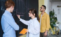 3 people staring at a chalkboard with a woman writing the word "recycling" on the chalkboard
