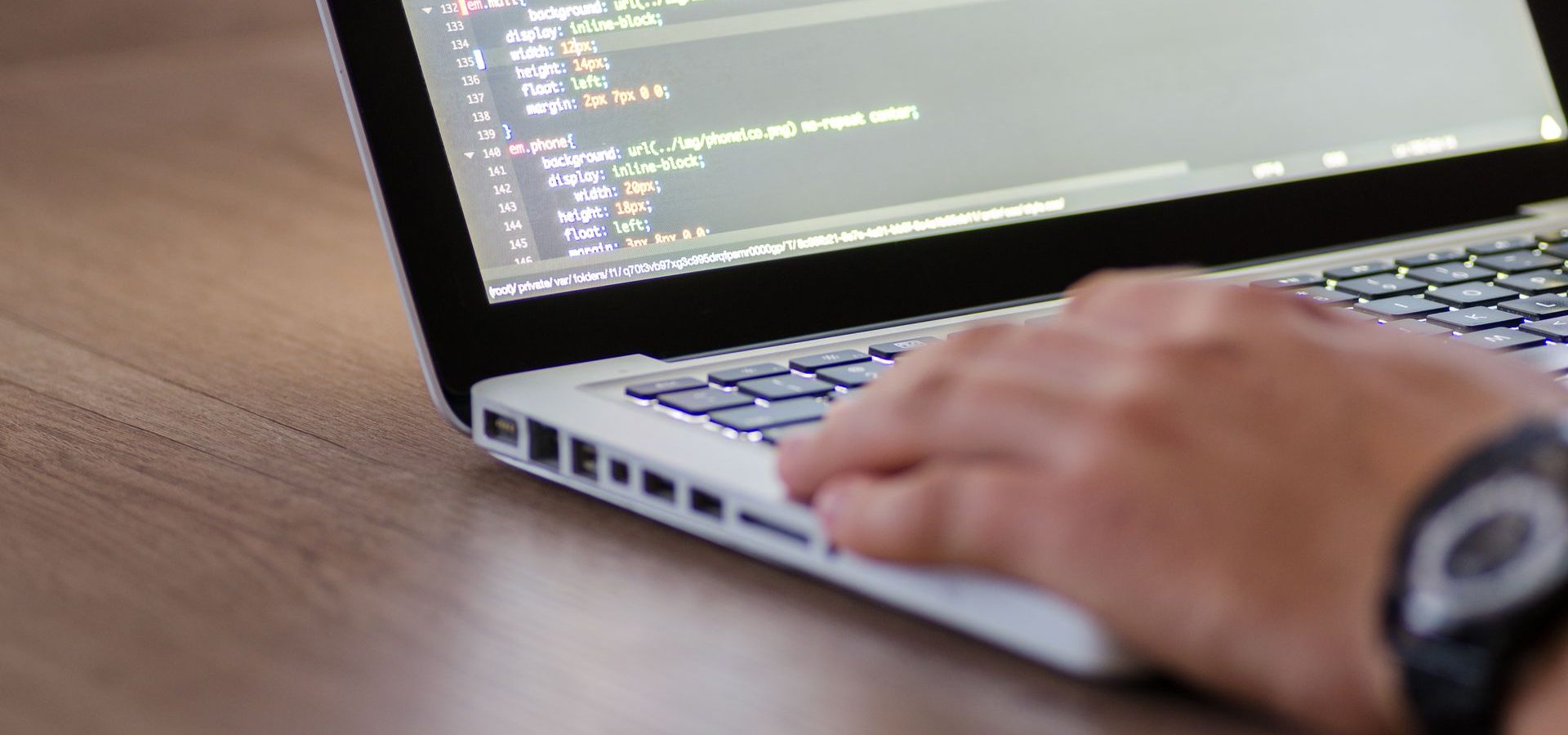Hand typing on laptop showing screen of codes