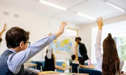 classroom with students facing away from camera with hands raised