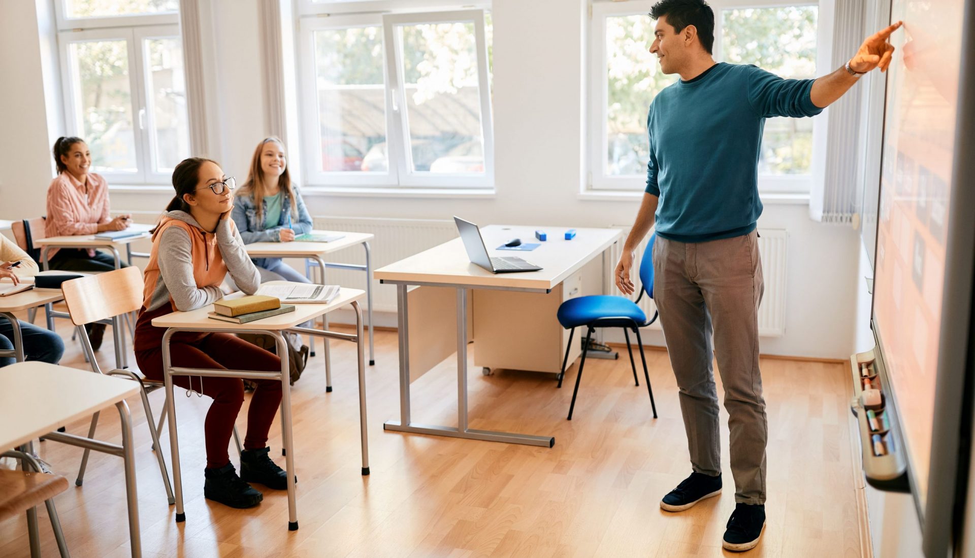 Teacher in front of classroom pointing at presentation