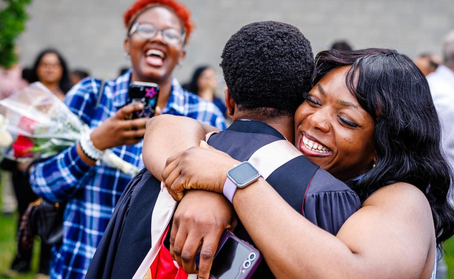Graduate in convocation regalia hugging a guest outdoors following a Brock University Convocation ceremony.