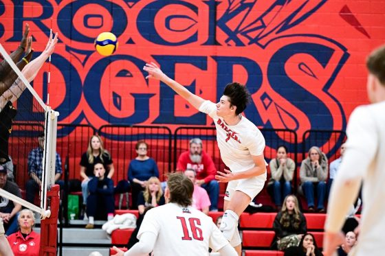Brock player in mid-jump for the volleyball that's coming over on their side of the net.