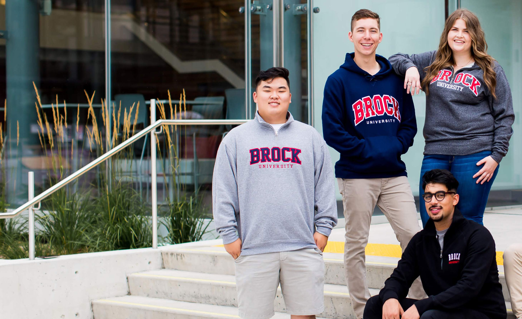 Students pose on the steps of Brock University wearing Brock branded hoodies and sweatshirts. 
